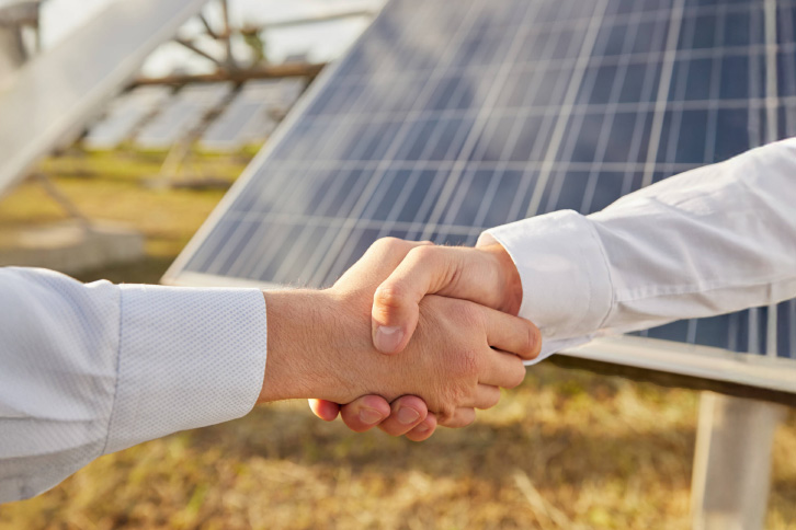 crop anonymous male business partners shaking hands as symbol agreement while standing near photovoltaic panels agricultural solar power station